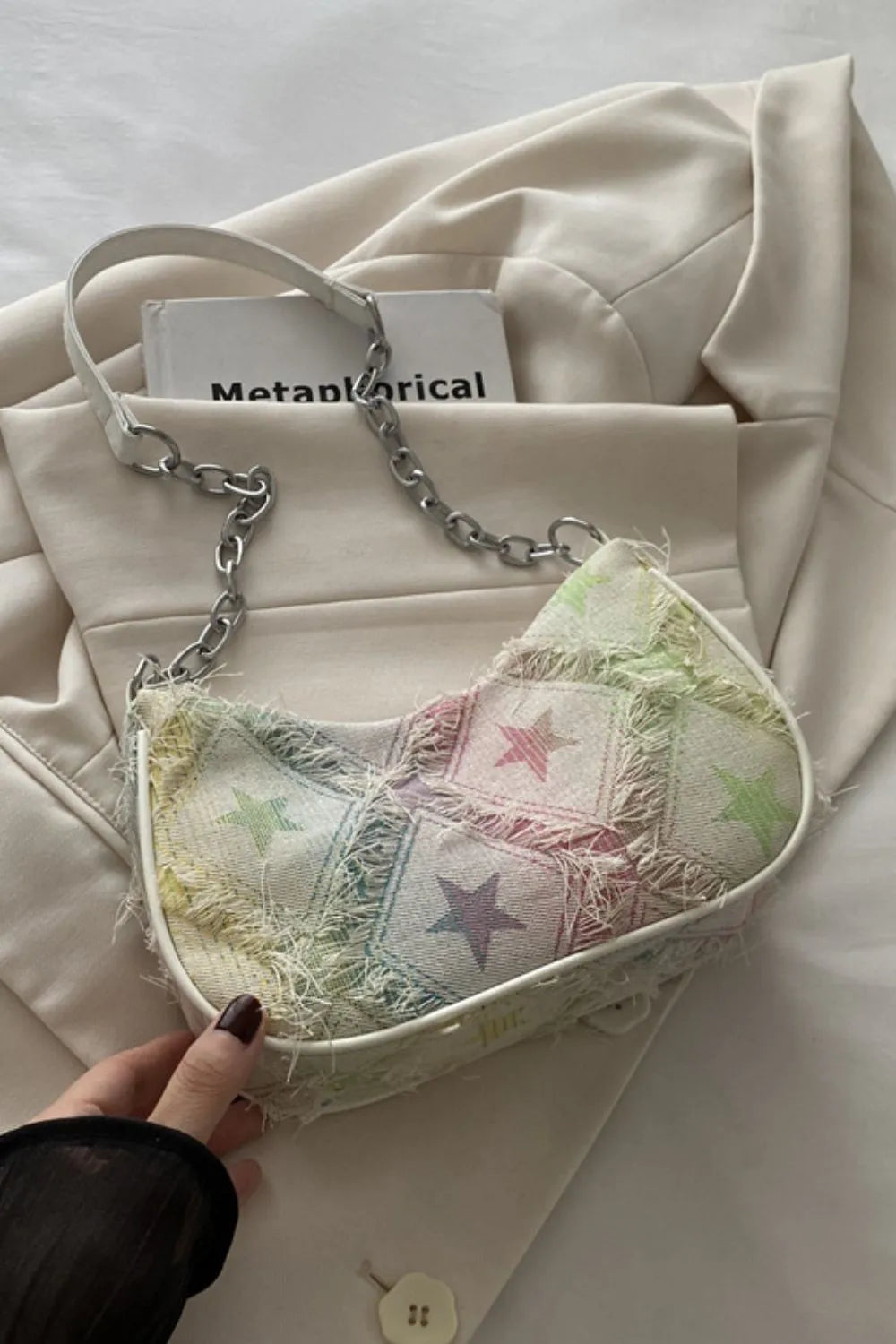 Rainbow starburst denim shoulder bag with frayed trim and chain strap.