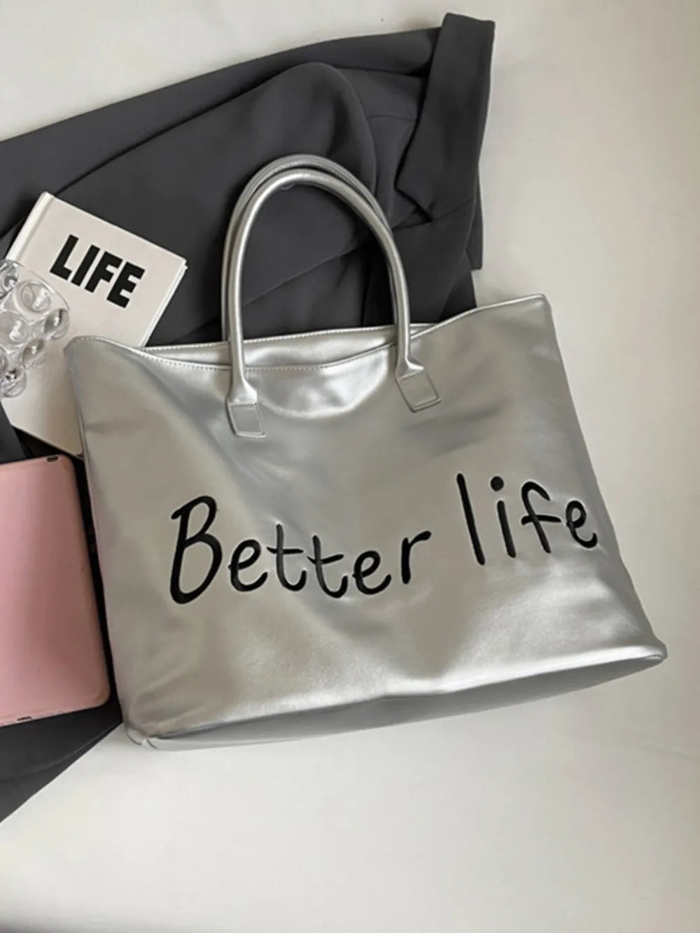 Silver tote bag with Better Life graphic and top handles.