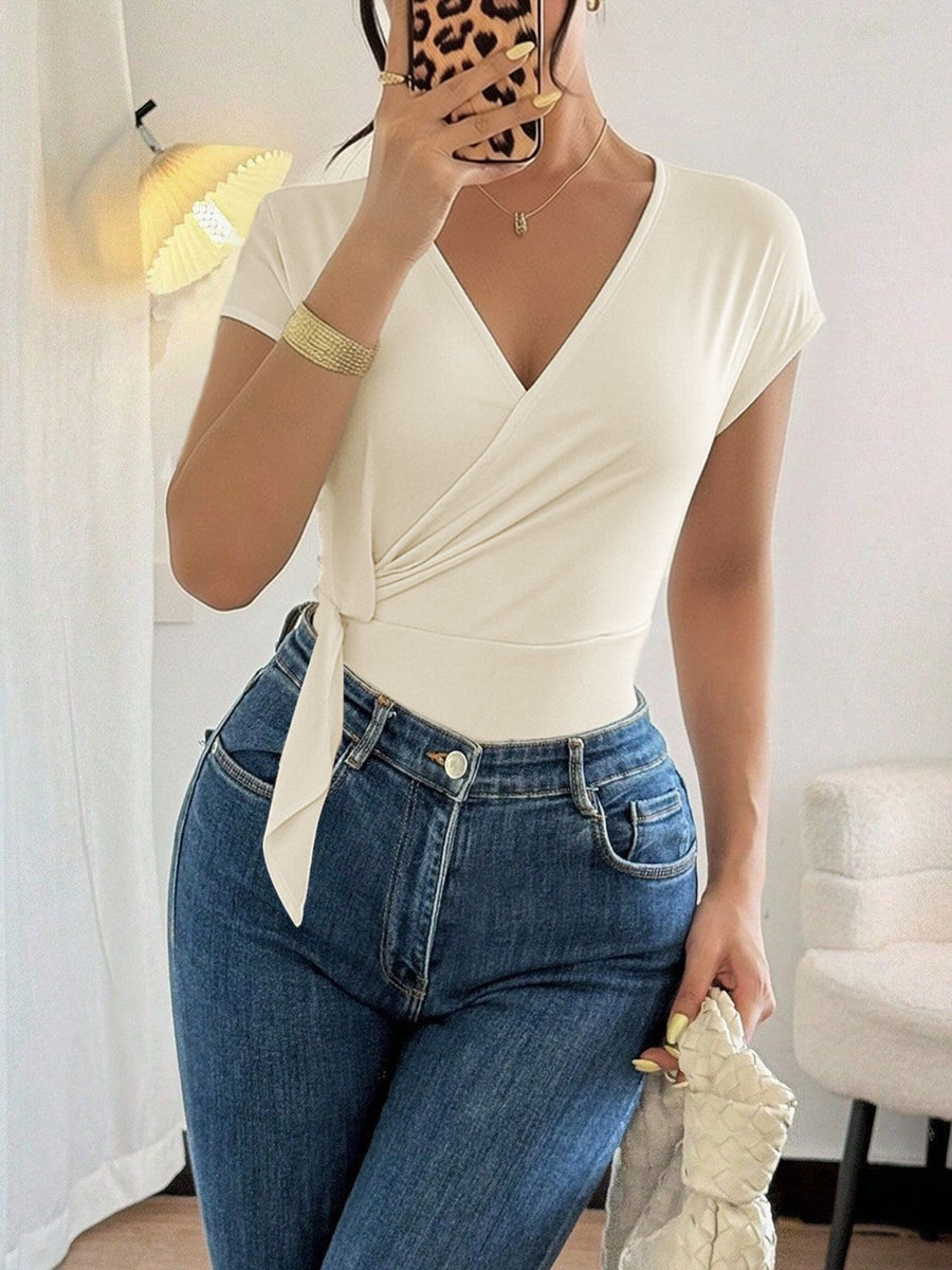 Cream surplice cap sleeve bodysuit with side tie detail, worn with blue jeans.