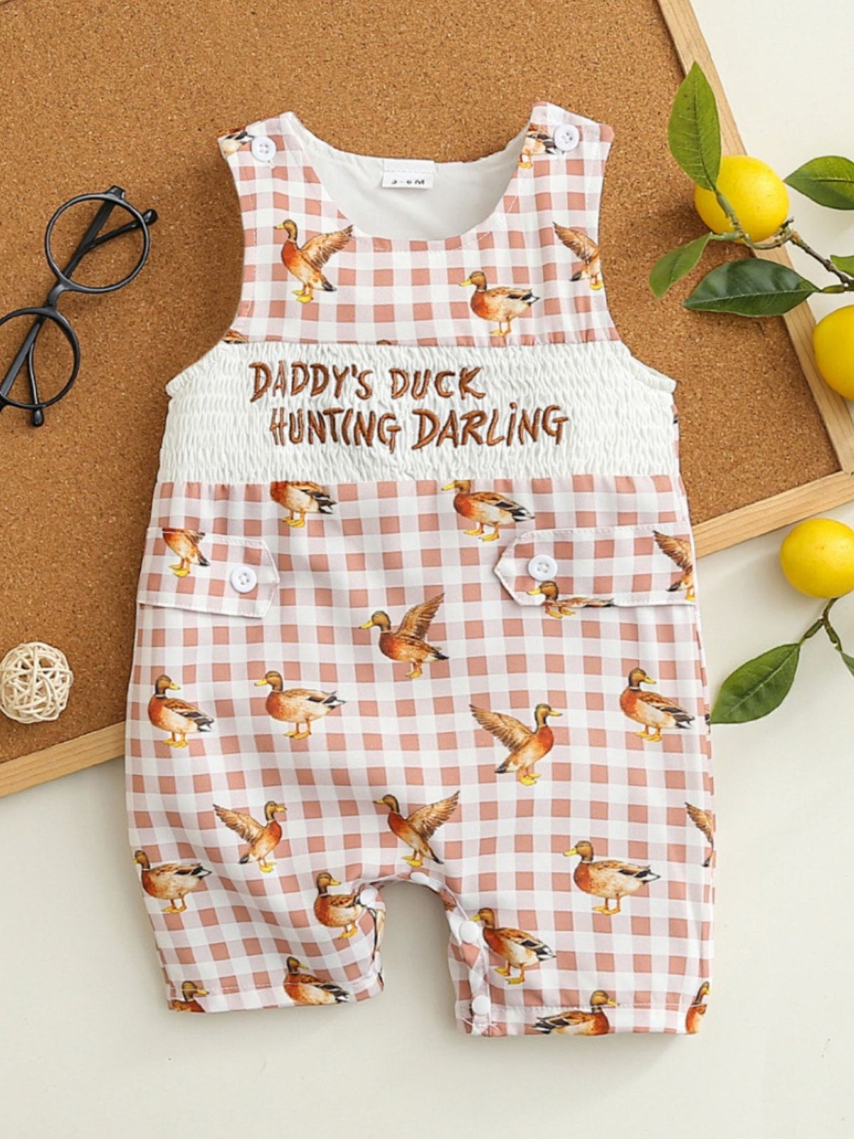Baby one-piece with duck print on pink gingham, smocked waist, and button details.