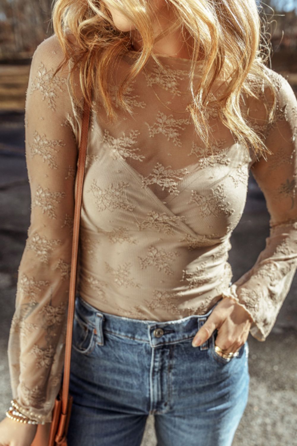 Tan floral lace bodysuit with long sleeves and a wrap neckline, worn with jeans.