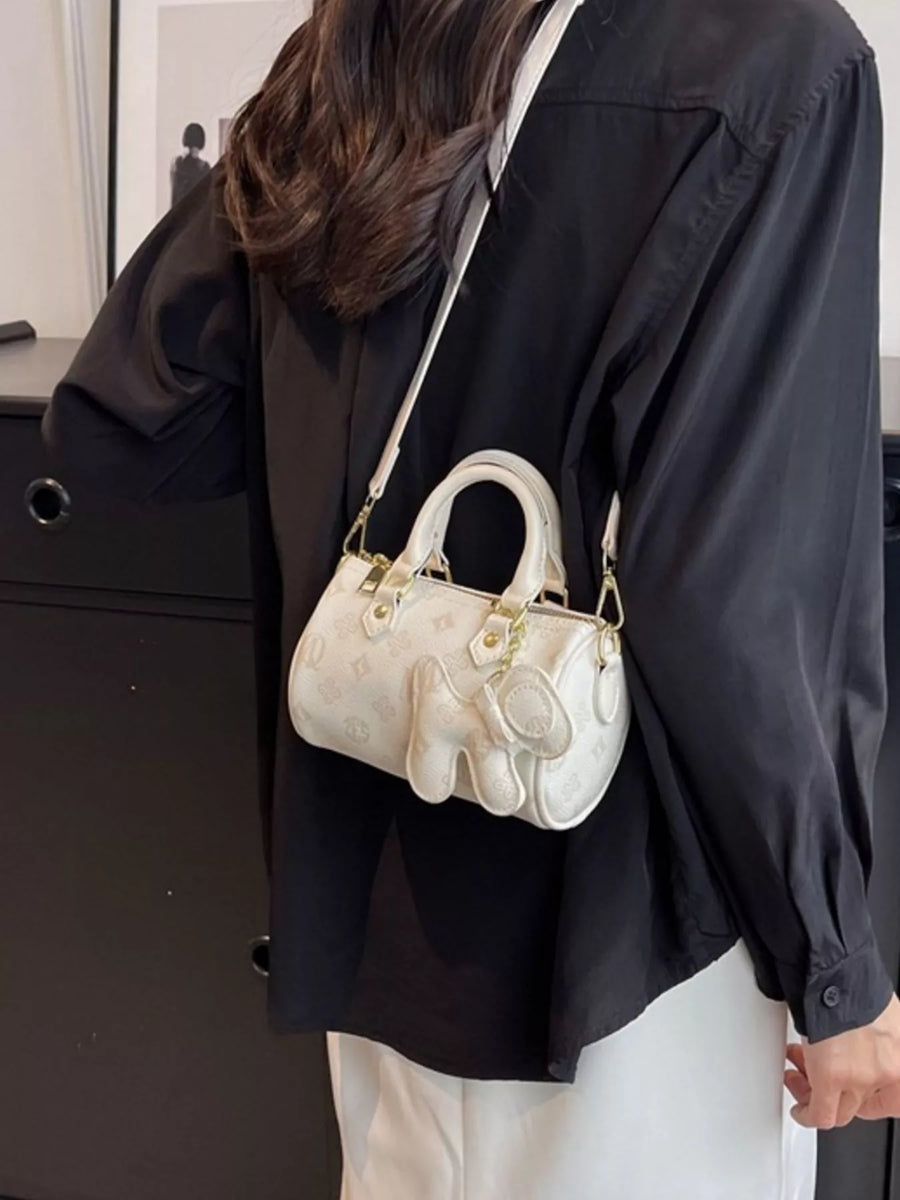 White mini barrel crossbody bag with embossed pattern and elephant charm detail