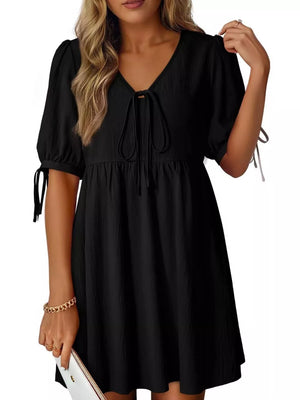 Black mini dress with tied neck, puff sleeves, and tie details on sleeves.