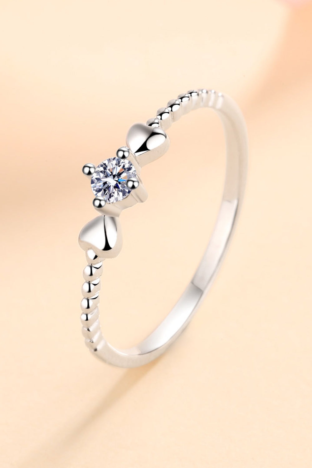 Silver ring with moissanite center stone and heart details on beaded band.