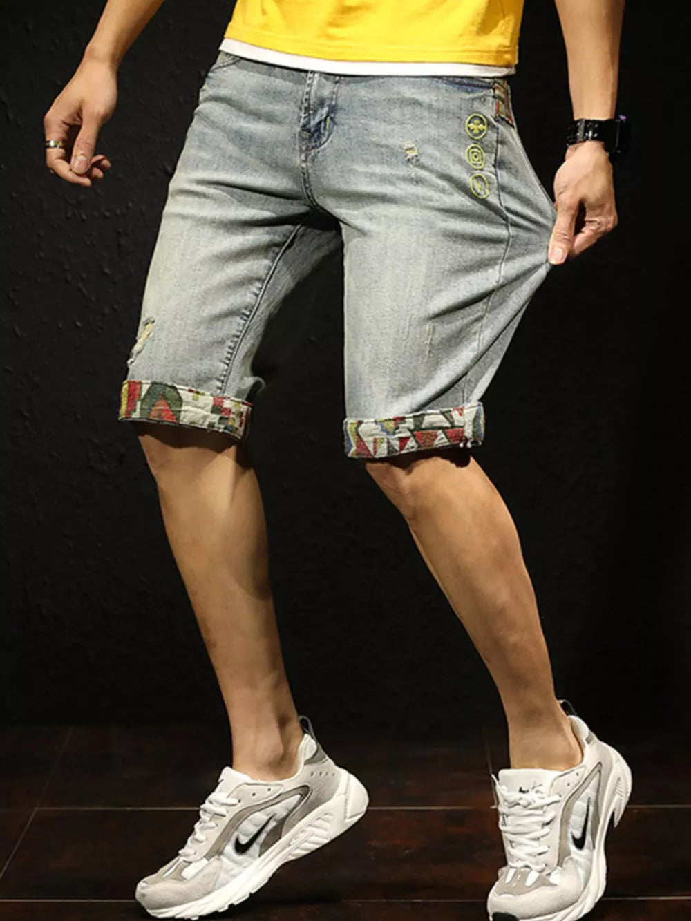 Men's light wash denim shorts with rolled cuffs featuring a colorful pattern and distressed details.