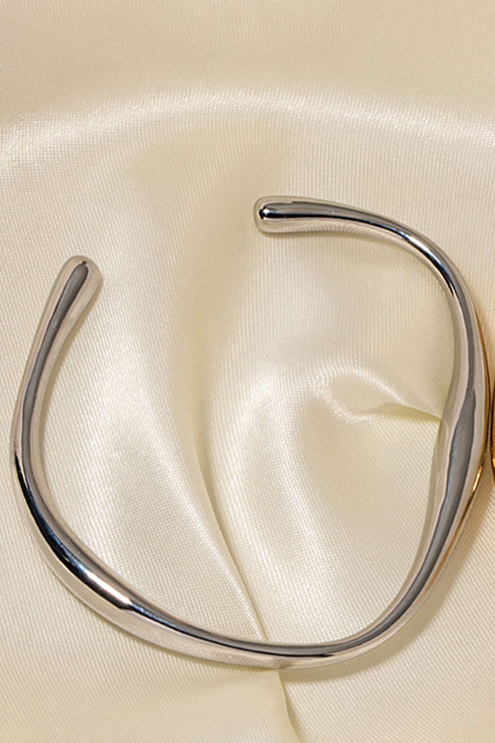 Sculpted silver open-ended bangle bracelet with a smooth, polished finish.