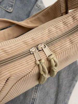 Beige corduroy shoulder bag with zipper detail and rope tassels.