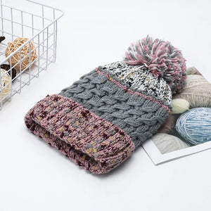 Textured cable knit beanie with a pink and gray pompom and a pink brim.