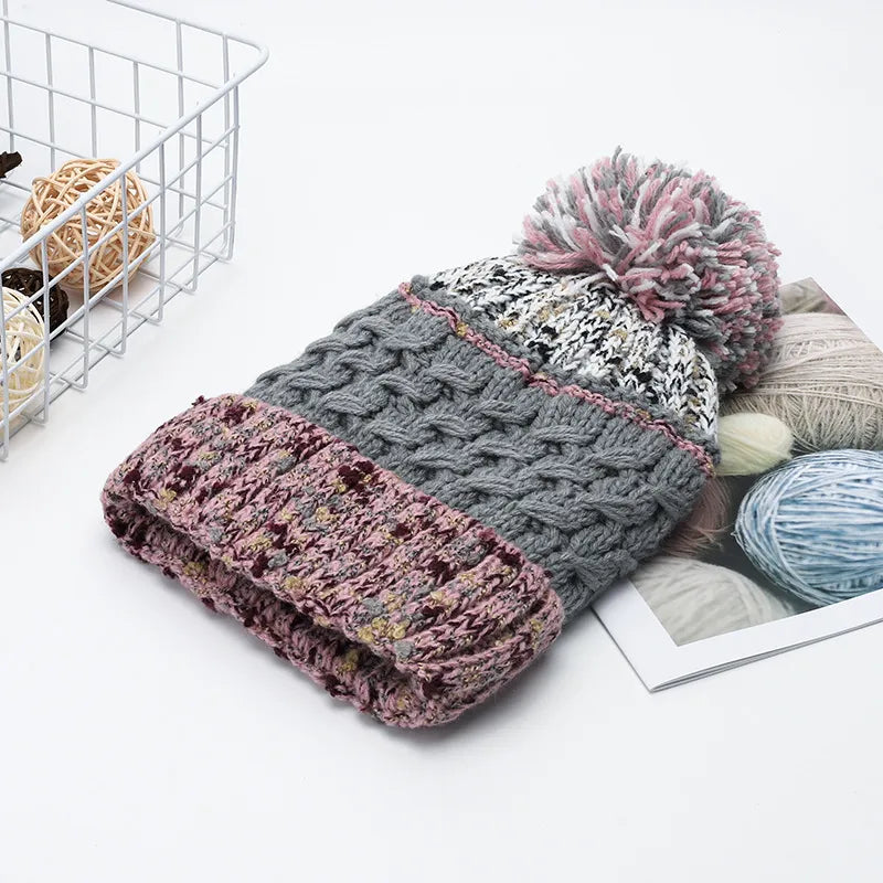Textured cable knit beanie with a pink and gray pompom and a pink brim.