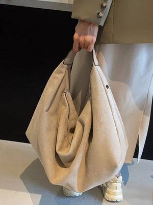 Spacious off-white suede shoulder bag with a front zipper pocket and top handles.