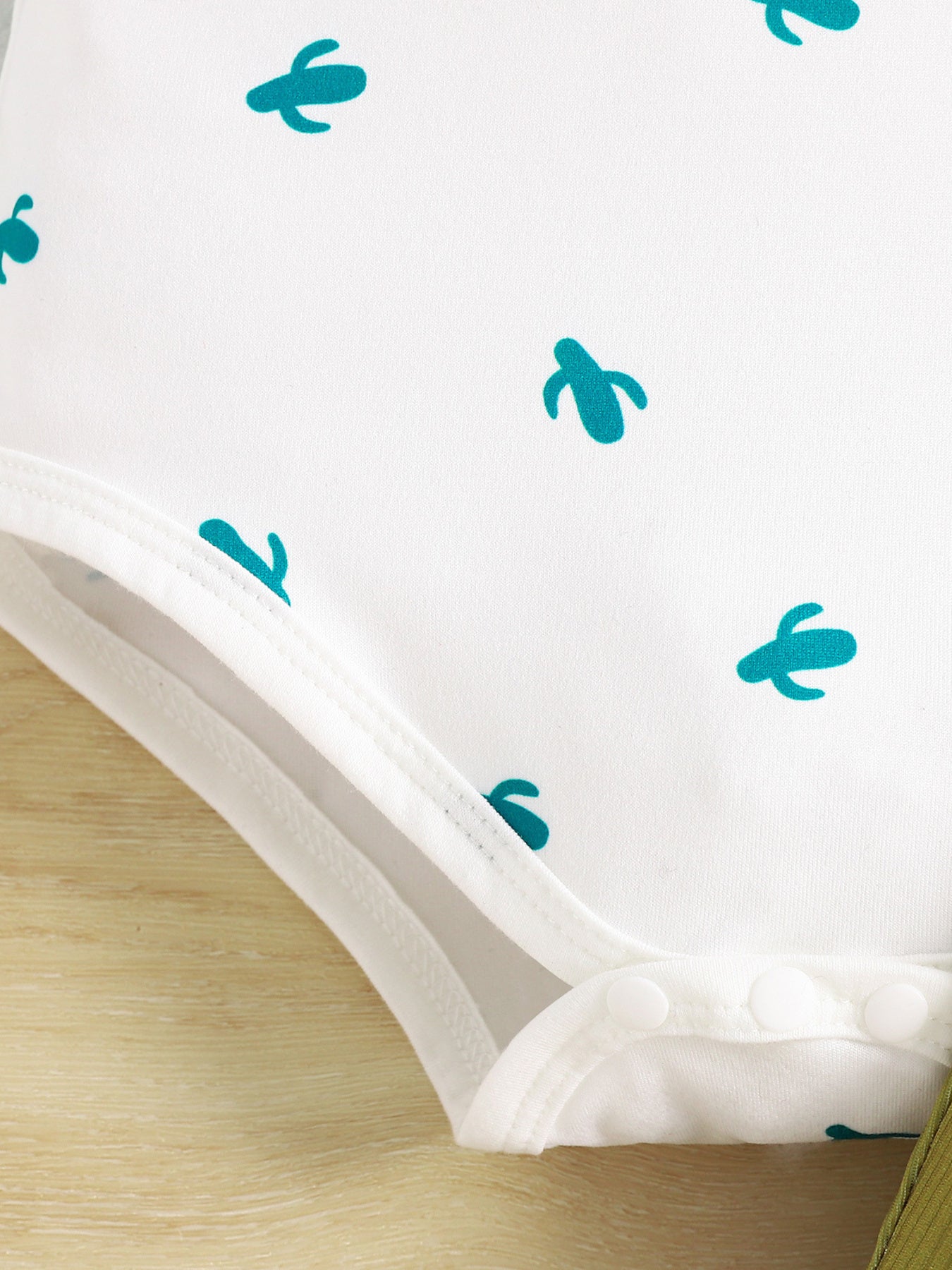 White baby bodysuit with teal cactus print and snap closure