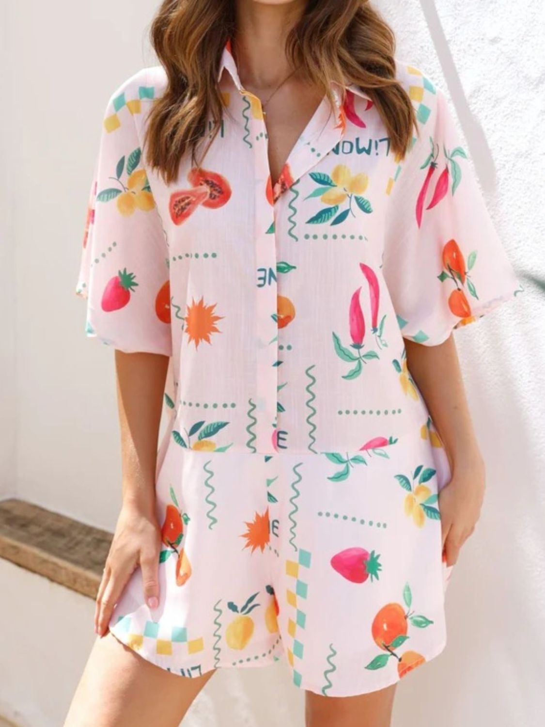 Blush pink romper with fruit and chili pepper print, short sleeves, collared neckline, button front.