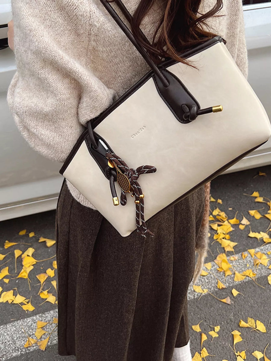 Beige leather shoulder bag with dark brown trim and a tennis racket charm.