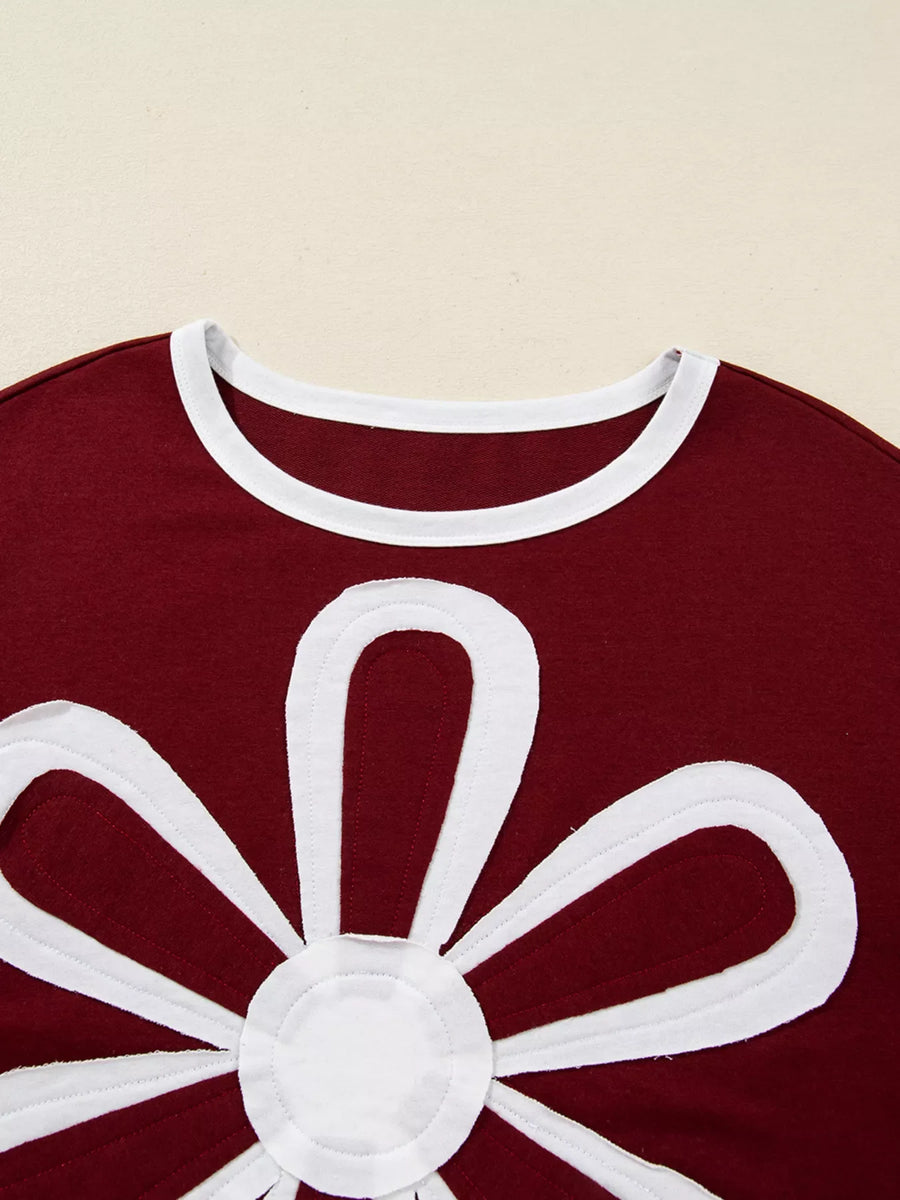 Burgundy long-sleeve top with white flower applique and contrast neckline.