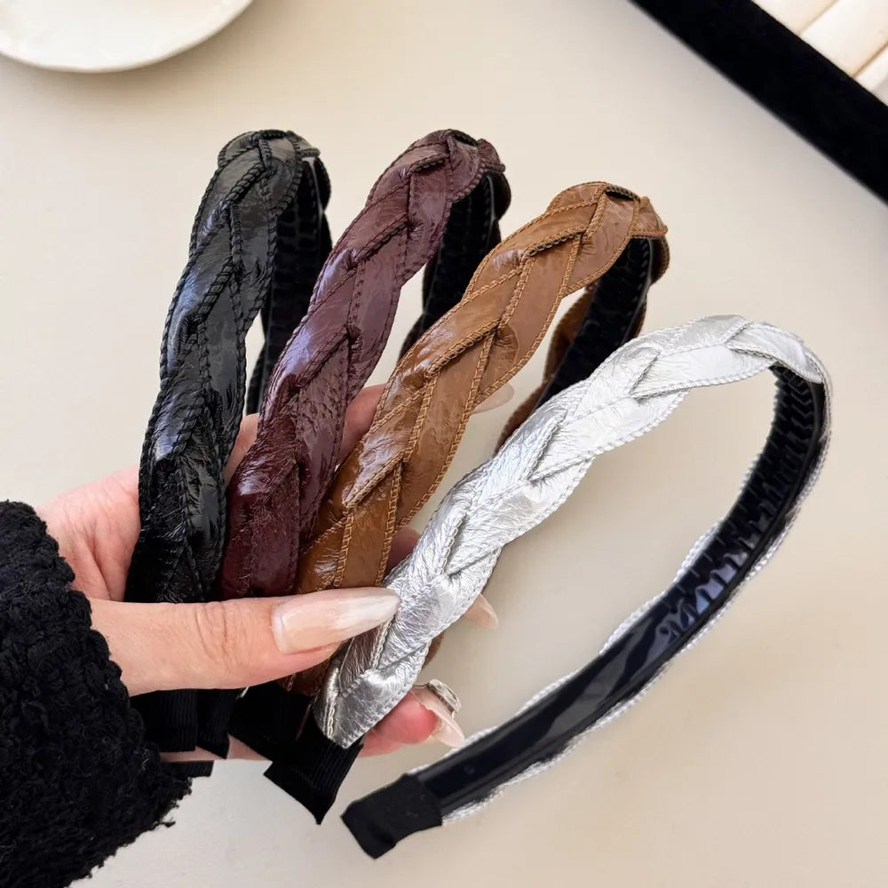 Woven faux leather headband in black, burgundy, camel, and silver with braided detail.