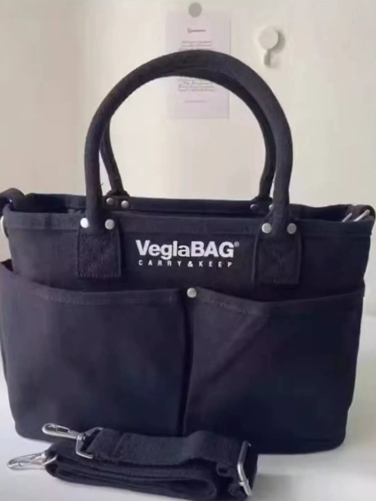 Black canvas shopper bag with multiple exterior pockets and top handles.