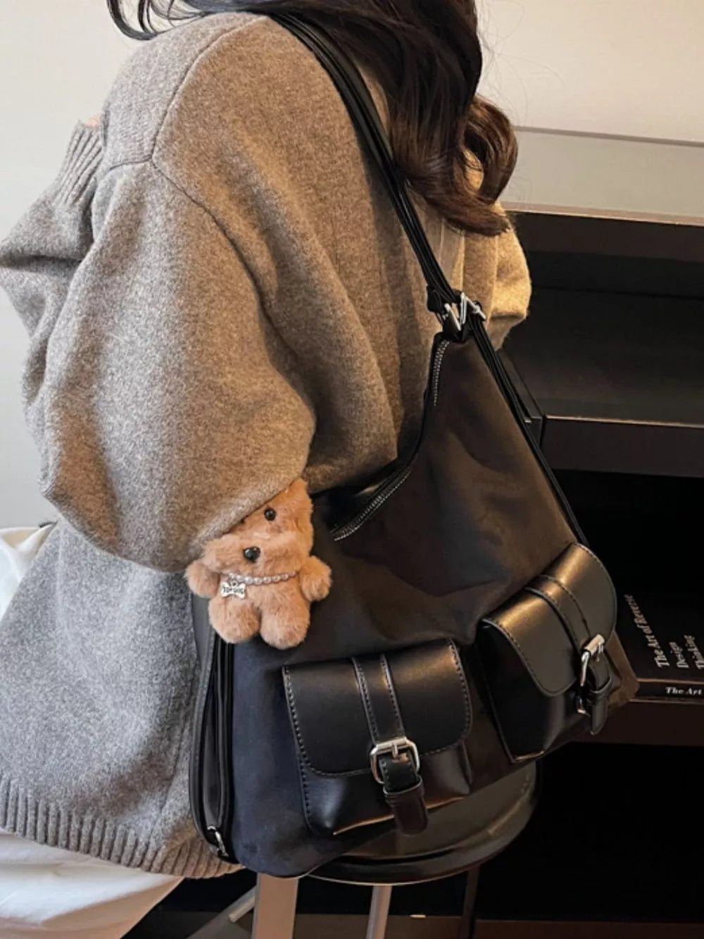 Black suede half-moon bag with multiple buckle pockets and a teddy bear charm.