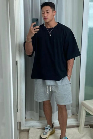 Black oversized drop-shoulder tee with short sleeves, paired with grey shorts.