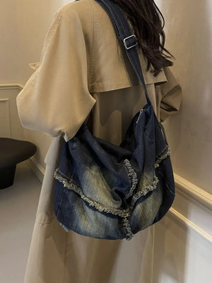 Frayed denim slouch crossbody bag in dark wash with distressed details and a casual style.