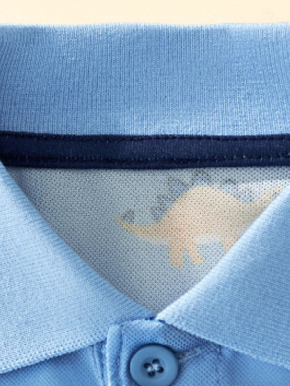 Light blue toddler polo shirt with a subtle dinosaur print inside the collar.