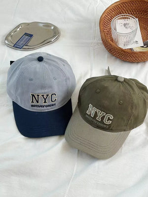 Cotton baseball caps with embroidered NYC detail, one grey with navy brim, one military green with grey brim.