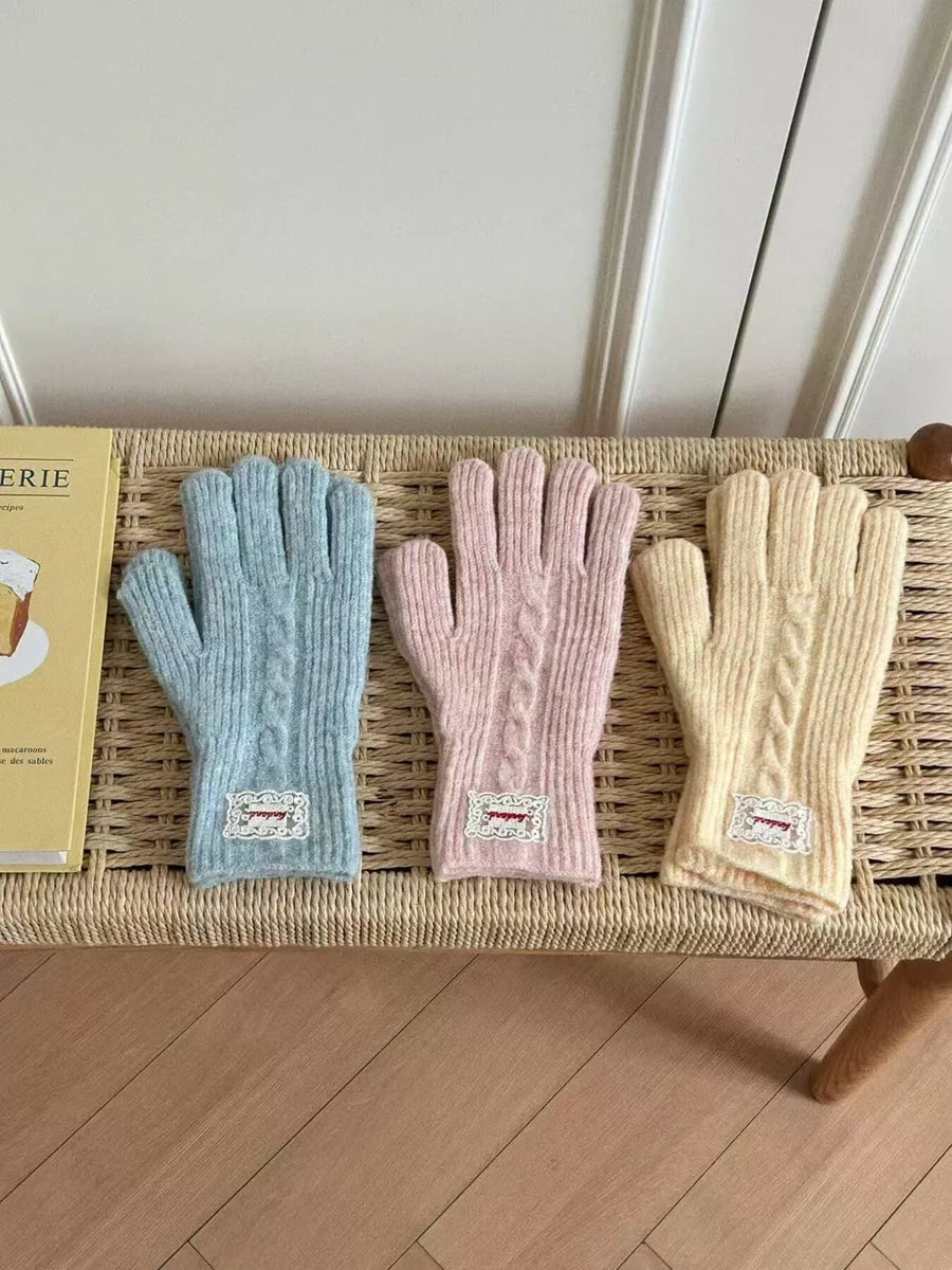 Cable knit gloves in blue, pink, and yellow with decorative patches.