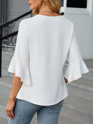 White V-neck blouse with ruffle sleeves and a textured fabric, styled with jeans.