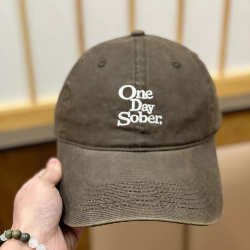 Brown baseball cap with white embroidered text "One Day Sober