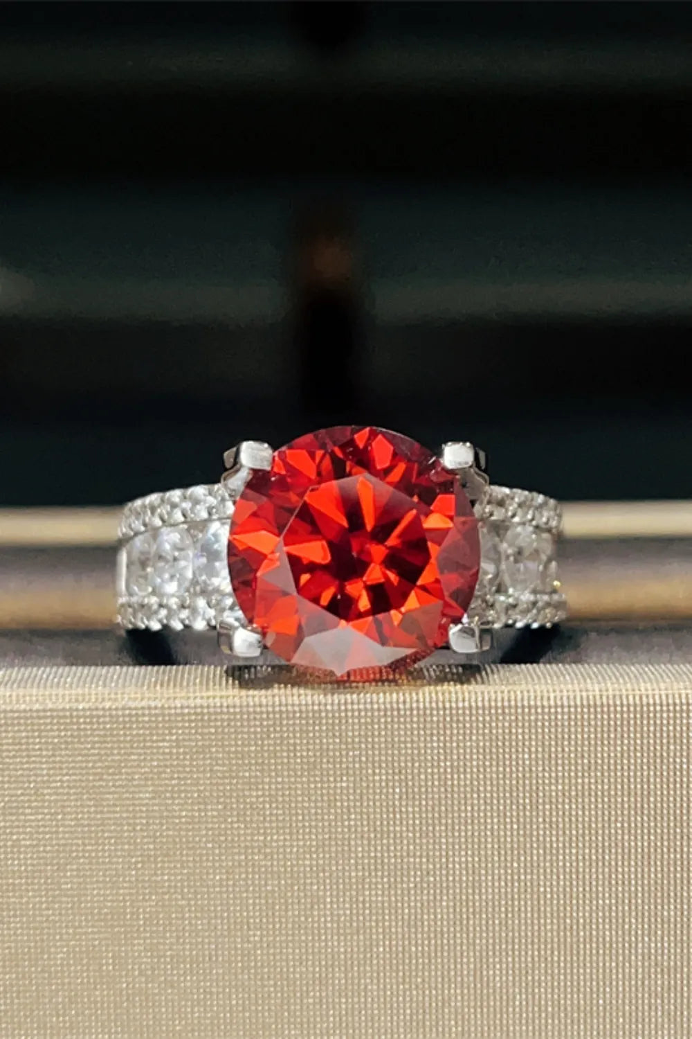 Crimson solitaire ring with pave band, featuring a large round red stone and small clear stones.