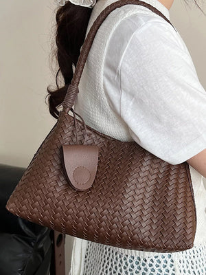 Woven shoulder bag in coffee color with braided strap and leather tab detail.