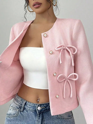 Pink textured jacket with pearl buttons and bow details, crew neck, long sleeves.