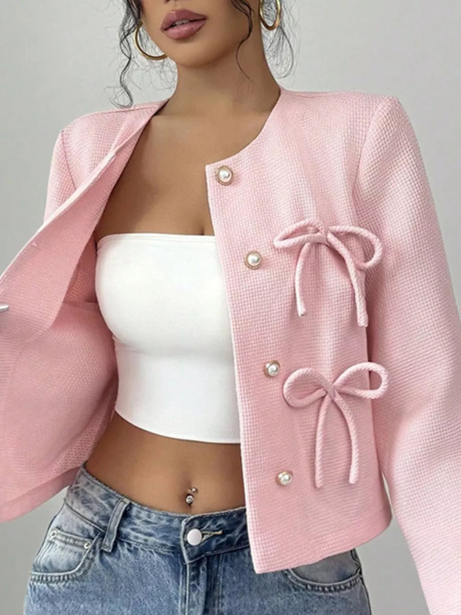 Pink textured jacket with pearl buttons and bow details, crew neck, long sleeves.