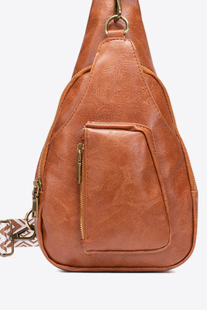 Brown textured sling bag with woven strap detail and front zip pocket.