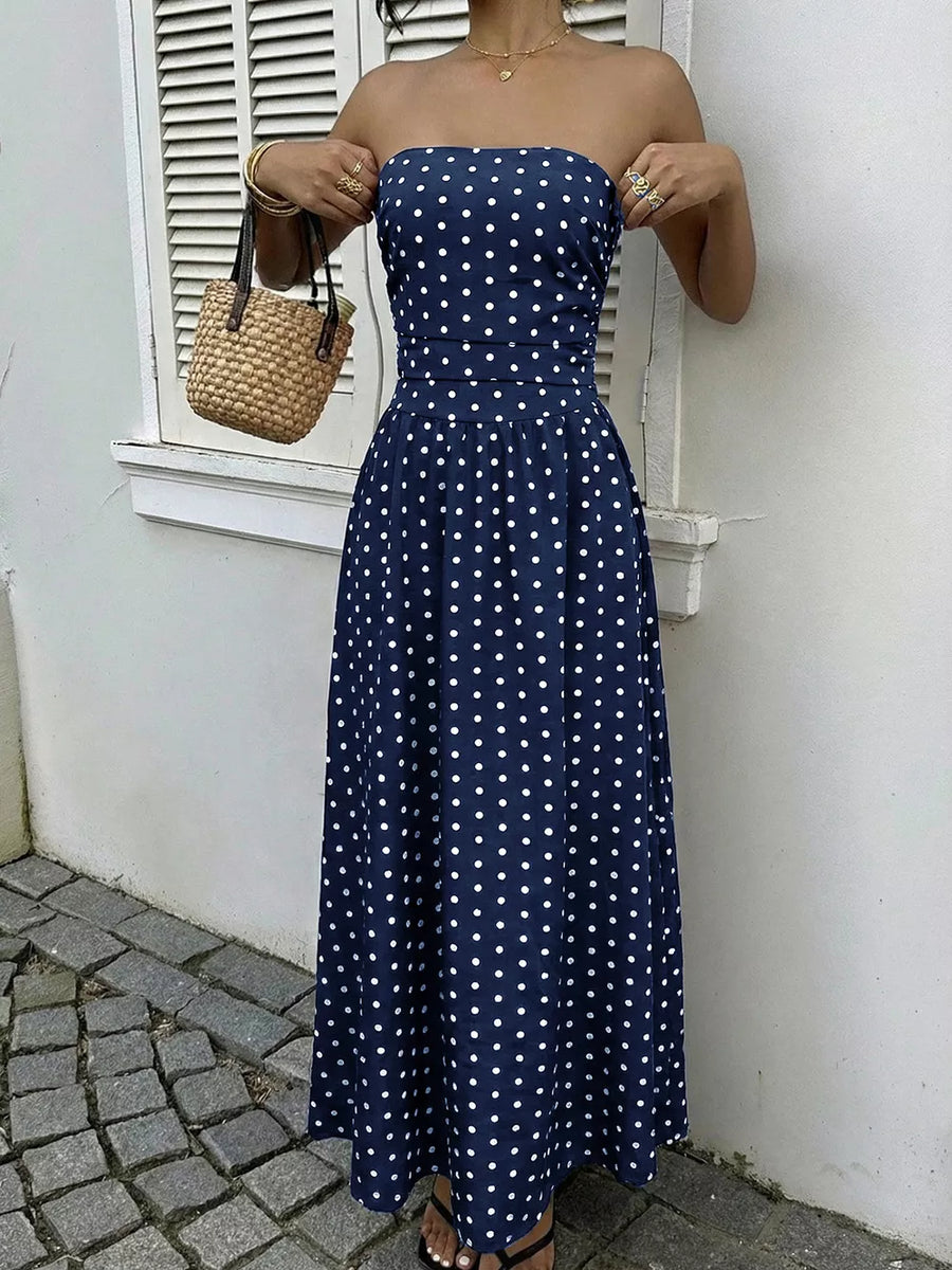 Navy polka dot A-line maxi dress with strapless neckline and cinched waist.