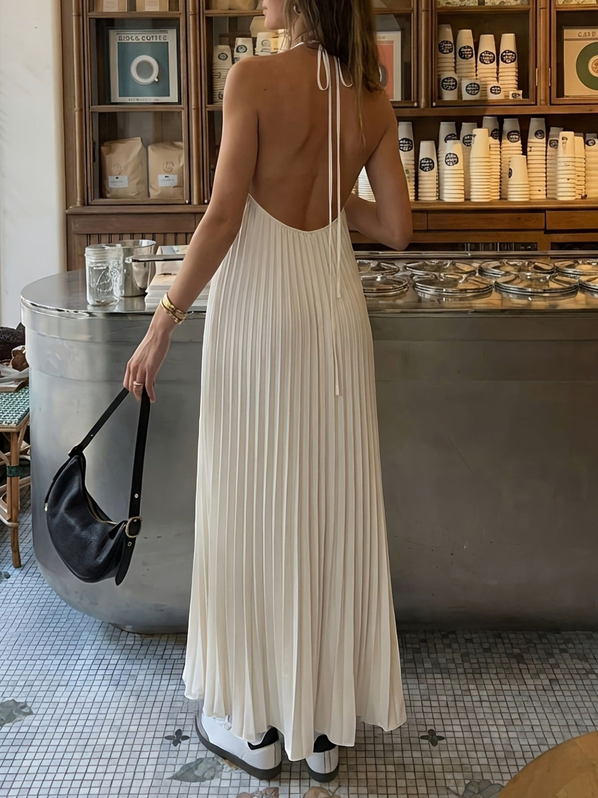 Backless pleated maxi dress in ivory with halter straps and a flowing skirt.