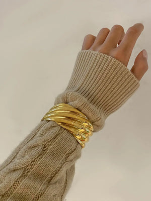 Gold cuff bracelet with sculpted wave detail on a cable knit sweater sleeve