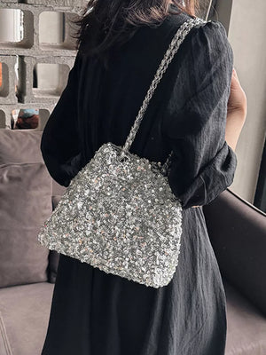Silver sequin bucket bag with chain strap worn by a person in a black dress.