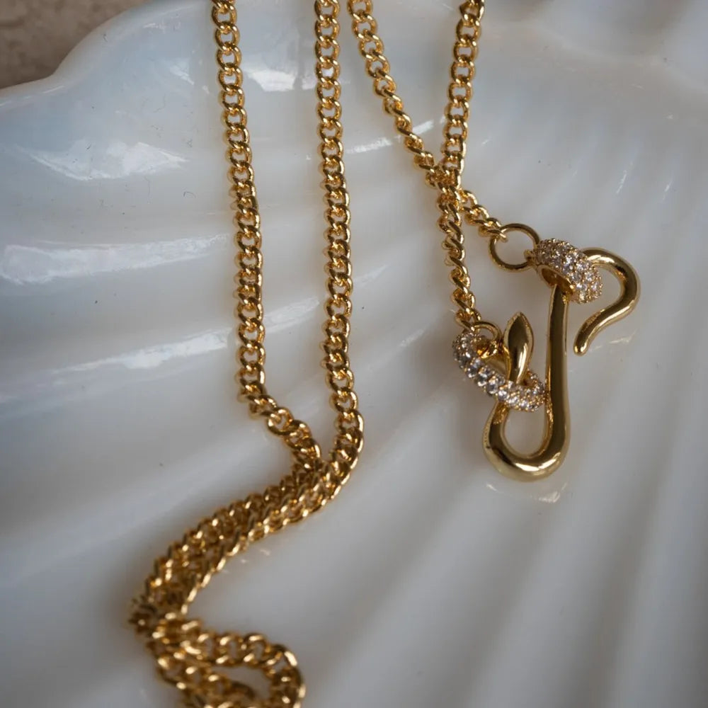 Gold curb chain necklace with a serpentine J initial pendant adorned with clear cubic zirconia stones.