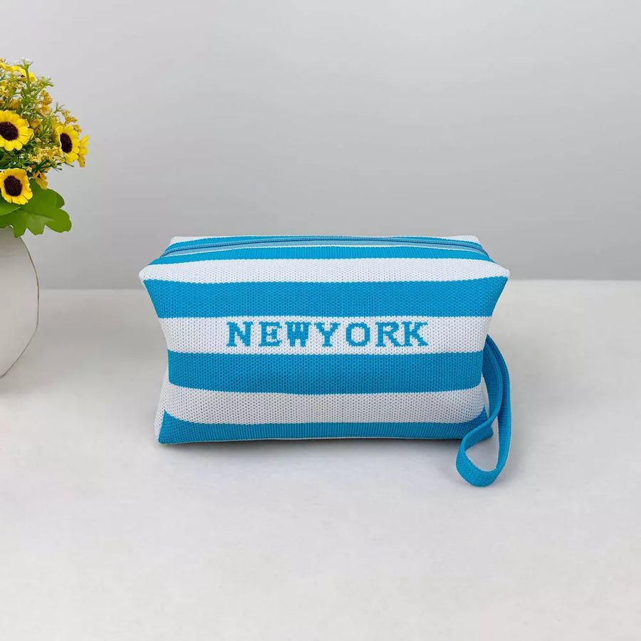 Striped small cosmetic bag in sky blue and white with NEW YORK text and a wrist strap.