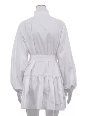 White cotton dress with ruffled neckline, balloon sleeves, belted waist, and tiered skirt.
