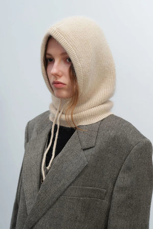 Beige knit balaclava with drawstring hood and ribbed trim, worn with a gray blazer.