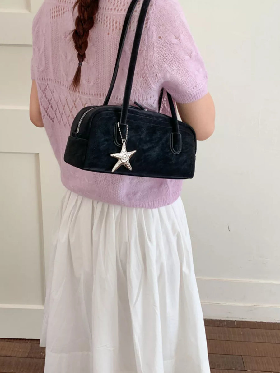 Black shoulder bag with star charm detail, styled with a lavender knit top and white skirt.