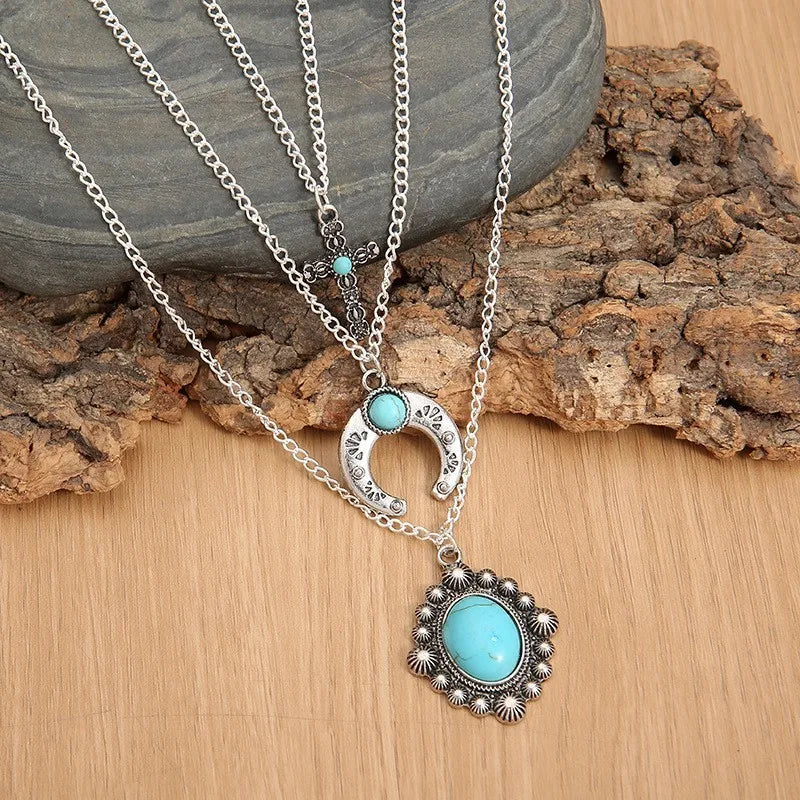 Silver layered pendant necklace with turquoise accents, featuring a horseshoe and floral charm.