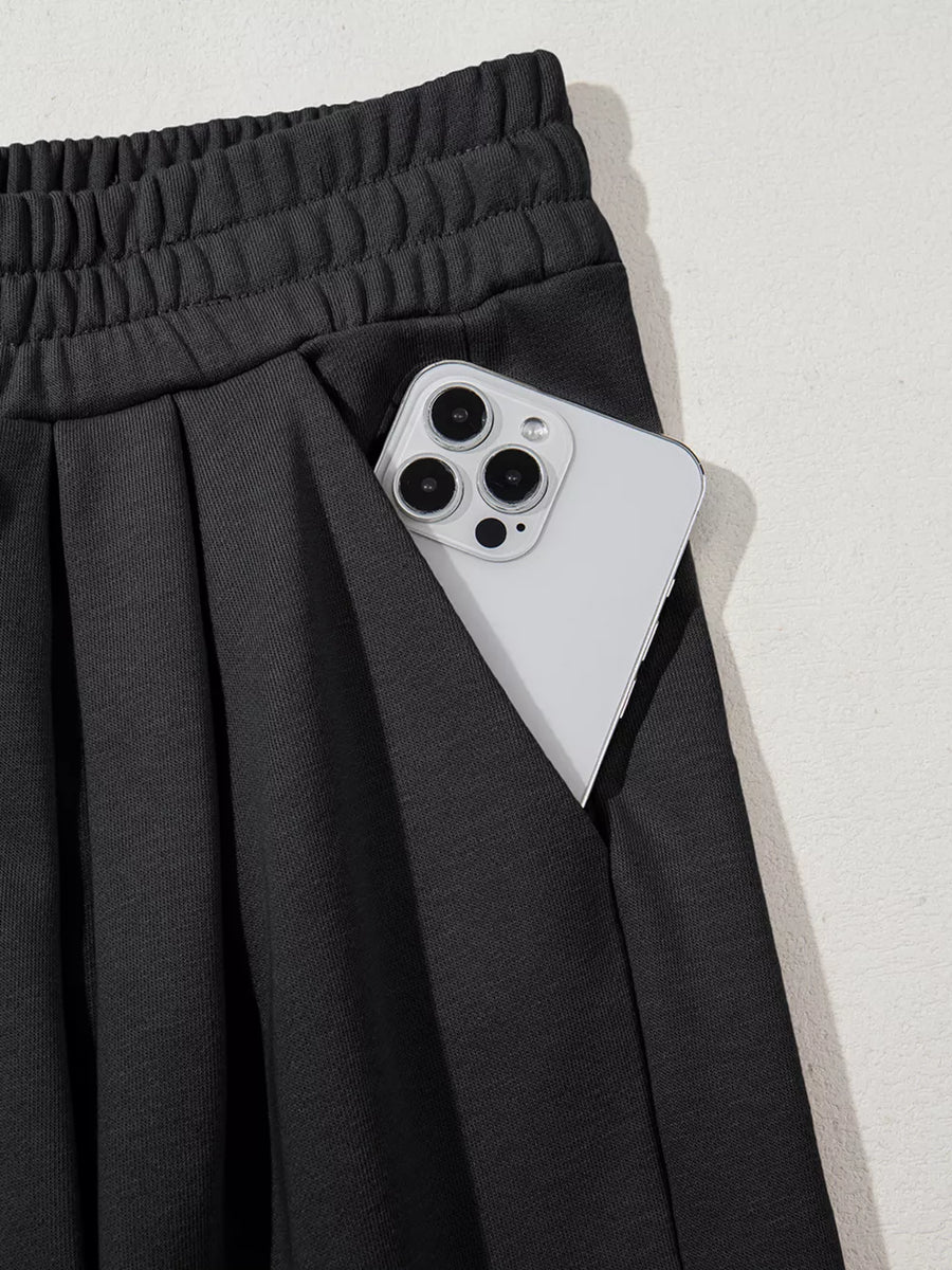 Black cotton maternity pants with drawstring waist, pleats, and a pocket holding a phone.