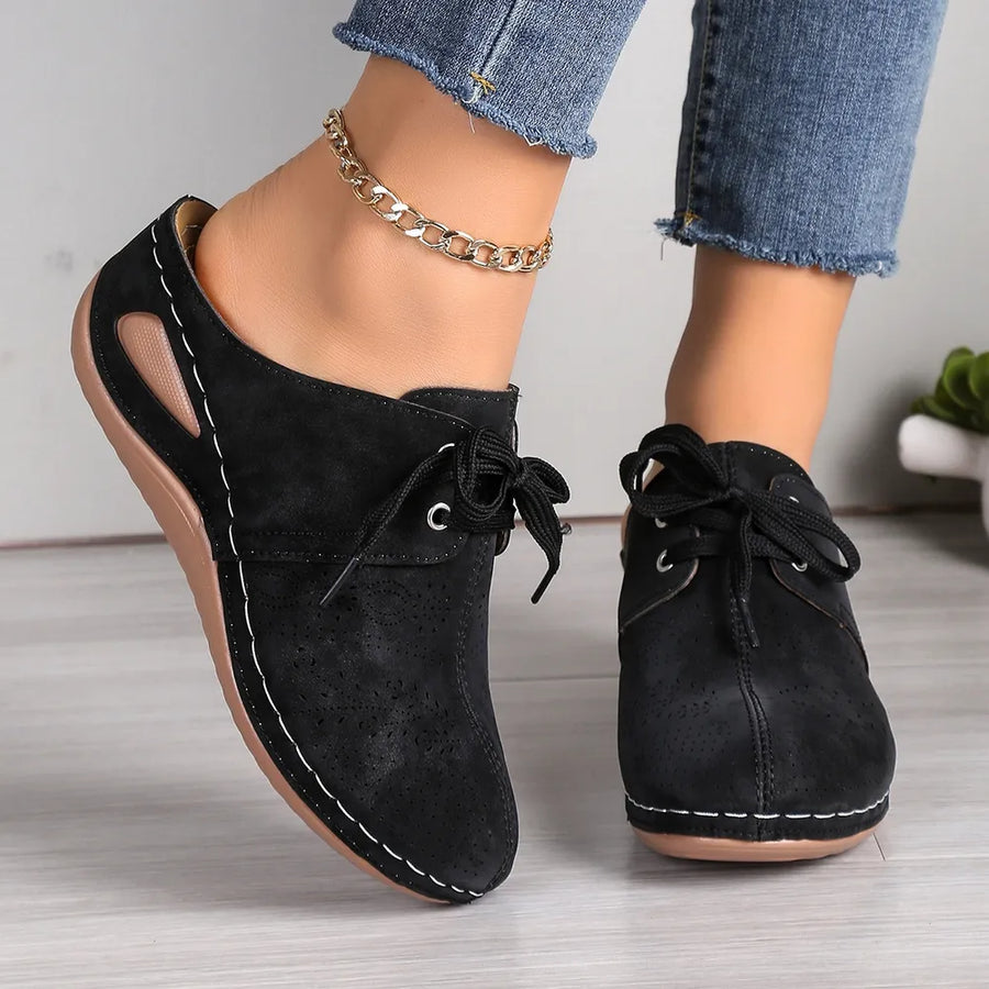 Black perforated lace-up mule flats with white stitching and side cutouts.