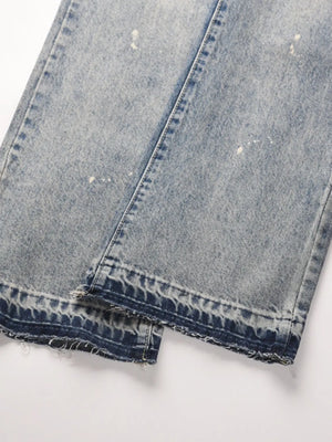 Distressed wash bootcut jeans with raw hem and paint splatters.