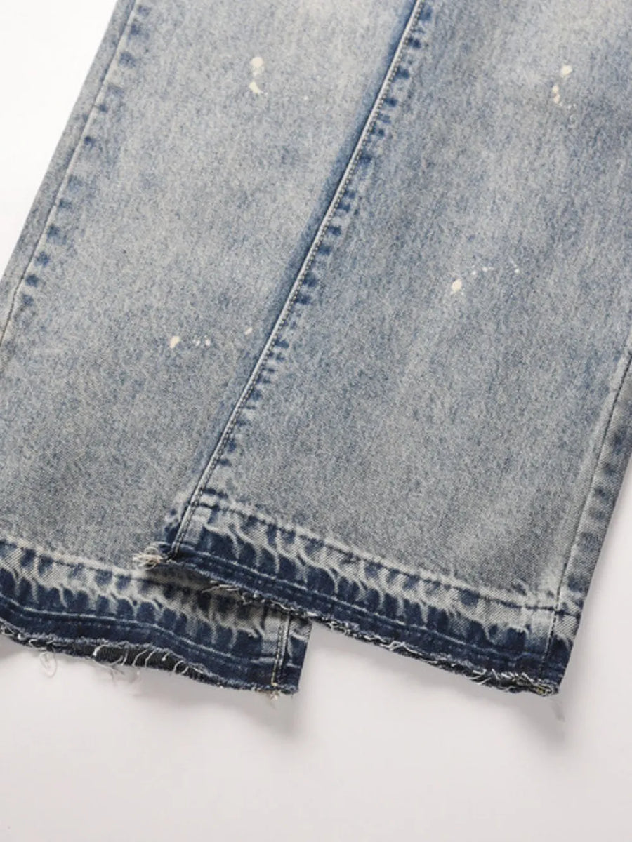 Distressed wash bootcut jeans with raw hem and paint splatters.