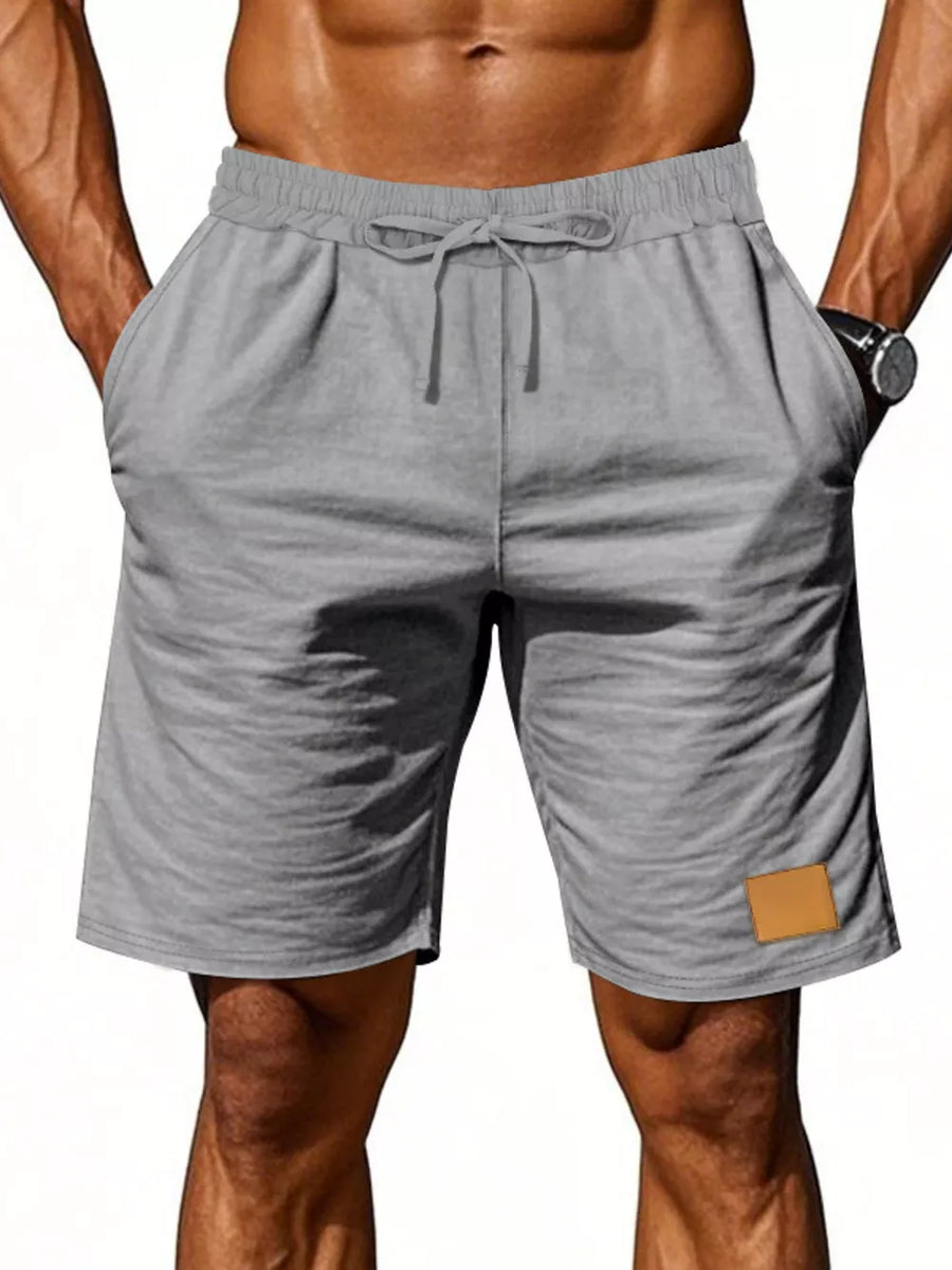 Light gray chino shorts with drawstring waist and leather patch detail.