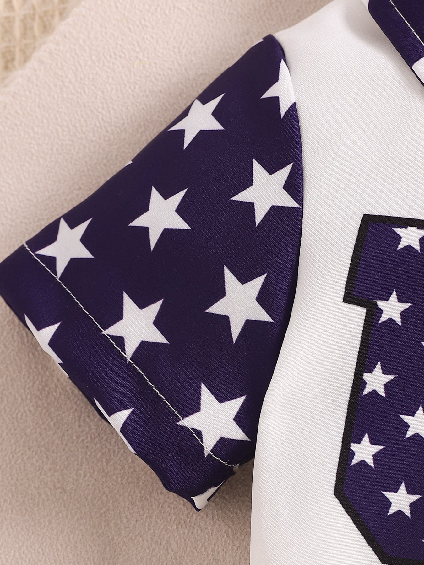 Baby bodysuit with navy sleeves and white stars, and a white front panel with a patriotic graphic.