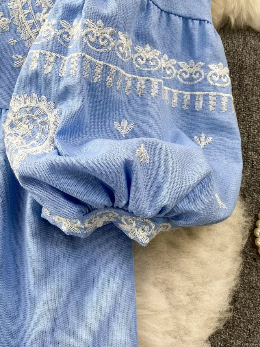 Blue balloon sleeve blouse with intricate white embroidery and tie neck detail.
